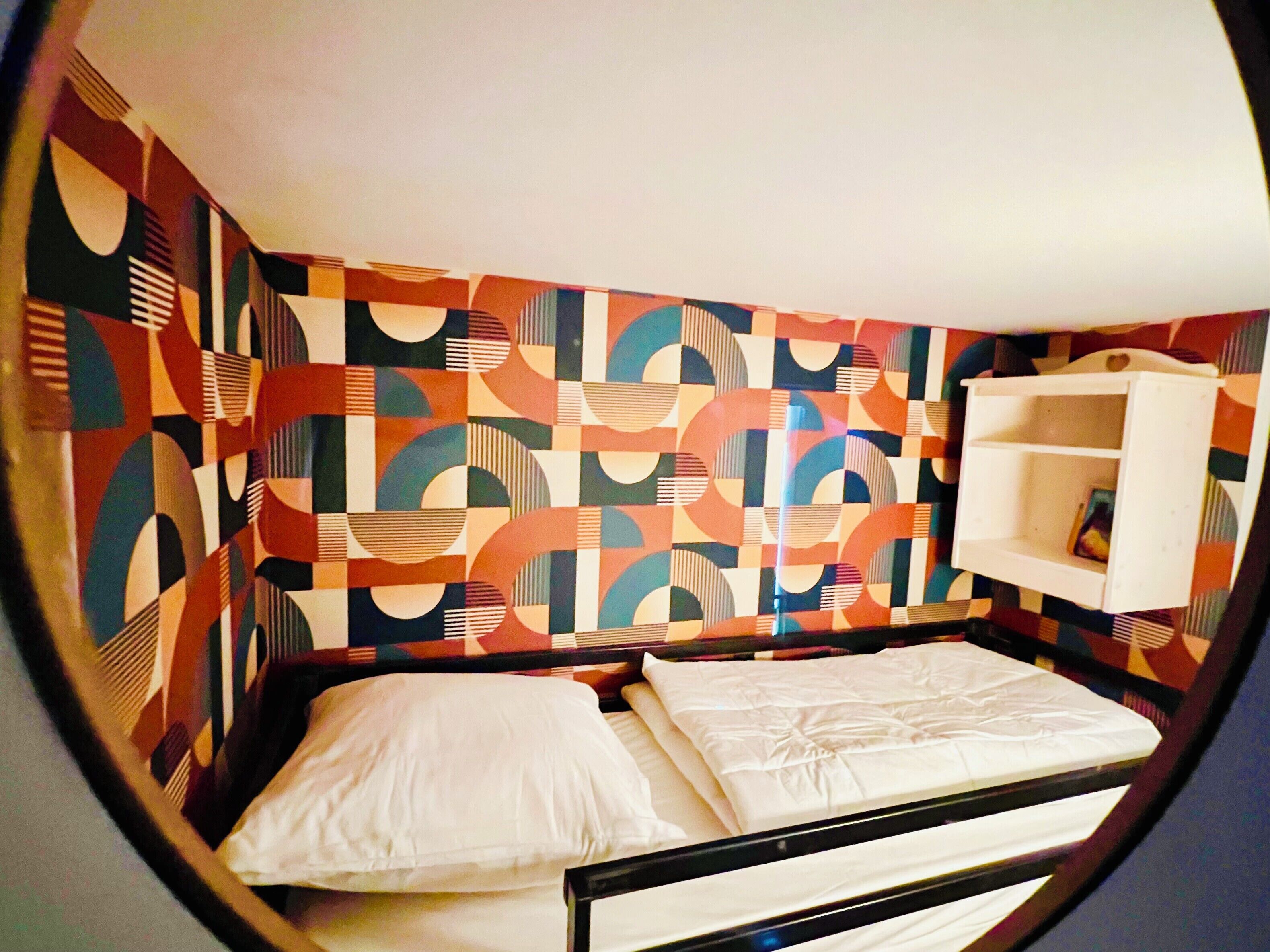 Quarto com uma cama, prateleira branca e parede estampada.