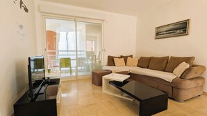 A living room with a brown sofa, a coffee table, a flat-screen TV, and a glass door leading to a balcony. - Apartment of 70 m with shared pool in Hyères (Hyères)