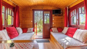 En hyggelig hytte med to senge i træ, et lille bord og et TV ophængt på væggen.