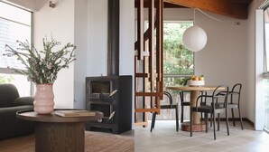 A modern living room with a wood-burning stove, a dining area with a round table and chairs, and a large window with a view of greenery. - Terrace Haus Margaret River (Margaret River)