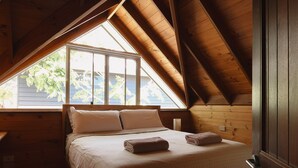 A bedroom with a sloped ceiling, a large window, and a bed with two pillows and two folded blankets. - Terrace Haus Margaret River (Margaret River)