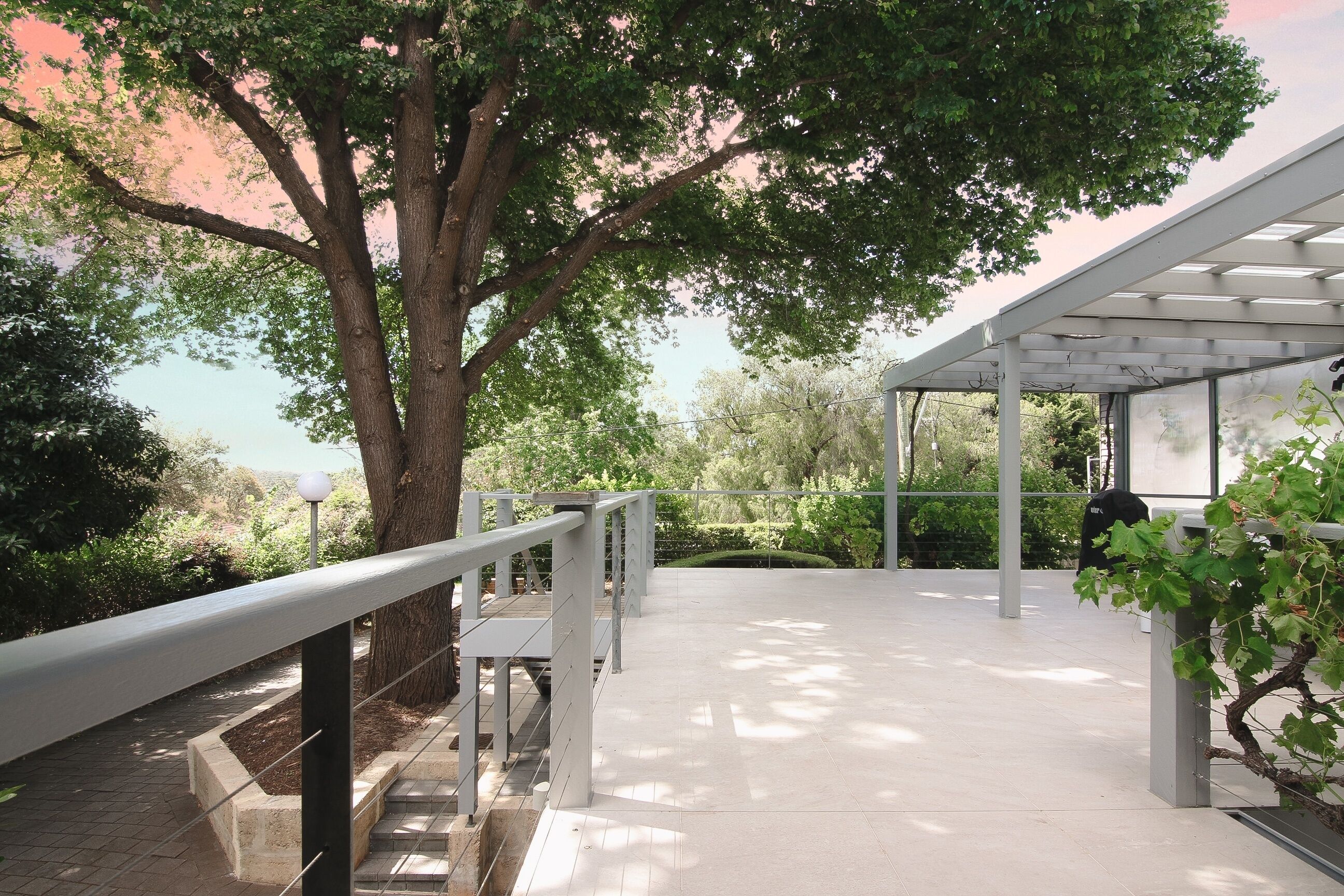A covered outdoor area with a metal railing, a tree, and a pergola structure.
