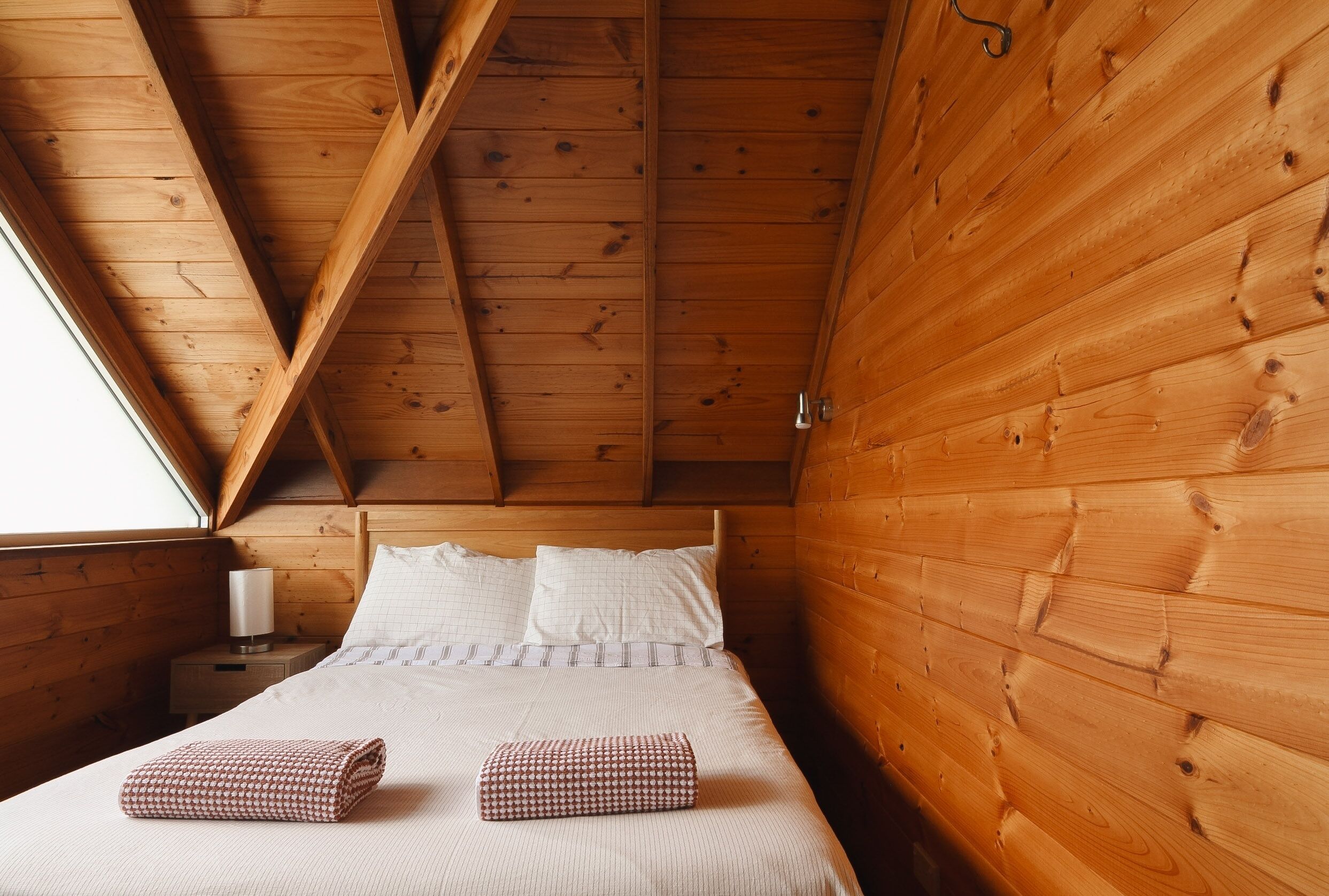 A wooden cabin bedroom with a bed, pillows, and a nightstand.