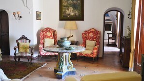 Une pièce comprenant deux fauteuils à motifs floraux, une table avec un vase, un tableau accroché au mur et un miroir qui reflète une autre pièce.