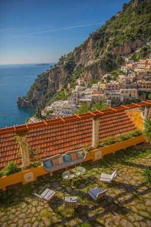 A terrace with stone flooring, a table with chairs, and a view of coastal buildings. - Villa la Pistrice (Positano)