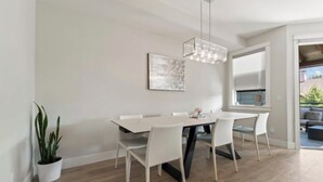 Een moderne eetruimte met een witte tafel en stoelen, een hanglamp en een potplant.