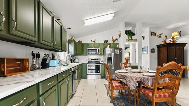 A kitchen with green cabinets, a microwave, stove, and a dining table with chairs. - Cozy 3BR Wheelchair Accessible Home with Private Pool Off US 192 Near Disney (Kissimmee)