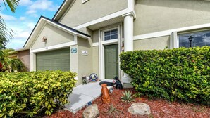 A residential house with a garage, a front door, and a well-maintained garden with mulch, rocks, and shrubs. - Cozy 3BR Wheelchair Accessible Home with Private Pool Off US 192 Near Disney (Kissimmee)