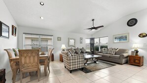 A spacious living room with a dining area, a ceiling fan, and a large window with blinds. - Cozy 3BR Wheelchair Accessible Home with Private Pool Off US 192 Near Disney (Kissimmee)