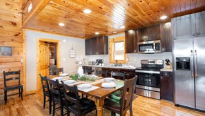 A wooden-paneled kitchen with a dining table set for four, stainless steel appliances, and a wooden ceiling. - Luxury Cabin w/Indoor Pool, Mini Golf & Mtn Views (Sevierville)