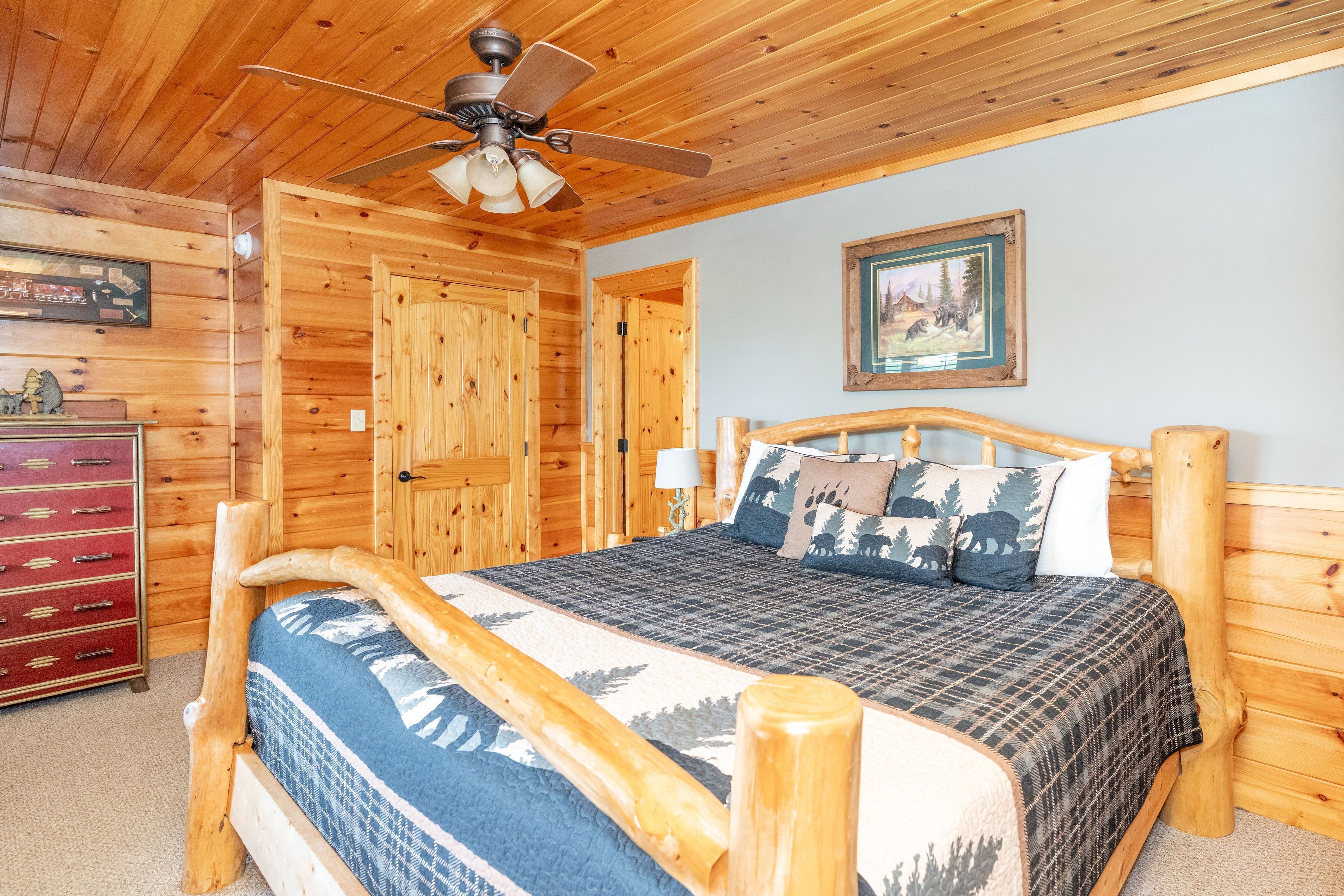A wooden cabin room with a bed, a ceiling fan, and a wooden dresser.