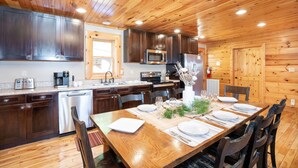 A wooden-paneled kitchen with a dining table set for four, equipped with modern appliances and a large window. - Luxury Cabin w/Indoor Pool, Mini Golf & Mtn Views (Sevierville)