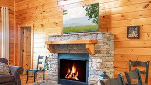 A cozy cabin interior with a stone fireplace, wooden walls, and a framed picture above the fireplace. - Luxury Cabin w/Indoor Pool, Mini Golf & Mtn Views (Sevierville)