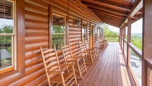 A covered porch with wooden benches and a railing, overlooking a scenic landscape. - Luxury Cabin w/Indoor Pool, Mini Golf & Mtn Views (Sevierville)