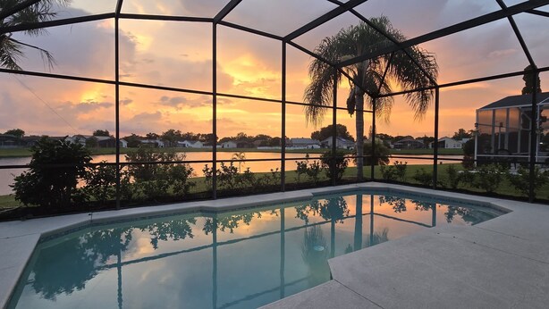 A swimming pool with a view of a sunset over a body of water, surrounded by greenery and a clear sky. - Modern Pool Home • Lake view (Kissimmee)