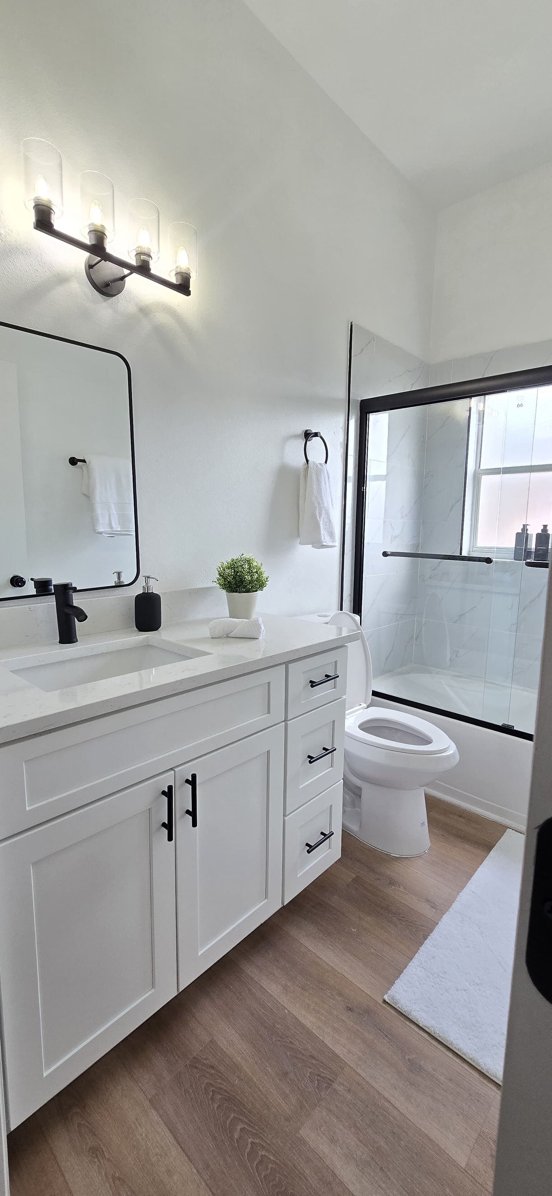 Ein modernes Badezimmer mit einem weißen Waschtisch, einem großen Spiegel, einer Glasdusche und einer weißen Toilette.