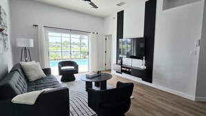 A modern living room with a sofa, chairs, a coffee table, and a TV mounted on the wall. - Modern Pool Home • Lake view (Kissimmee)