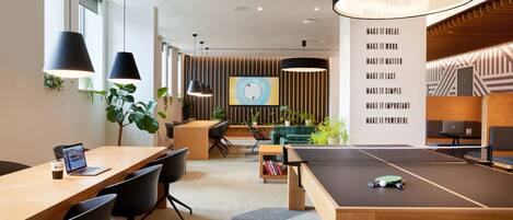 A modern office space with a ping pong table, meeting tables, and a large wall with motivational quotes.
