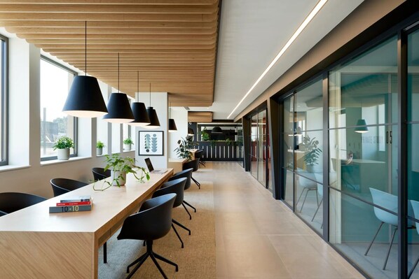 Un espacio de oficina moderno con una larga mesa de madera, sillas negras e iluminación colgante.