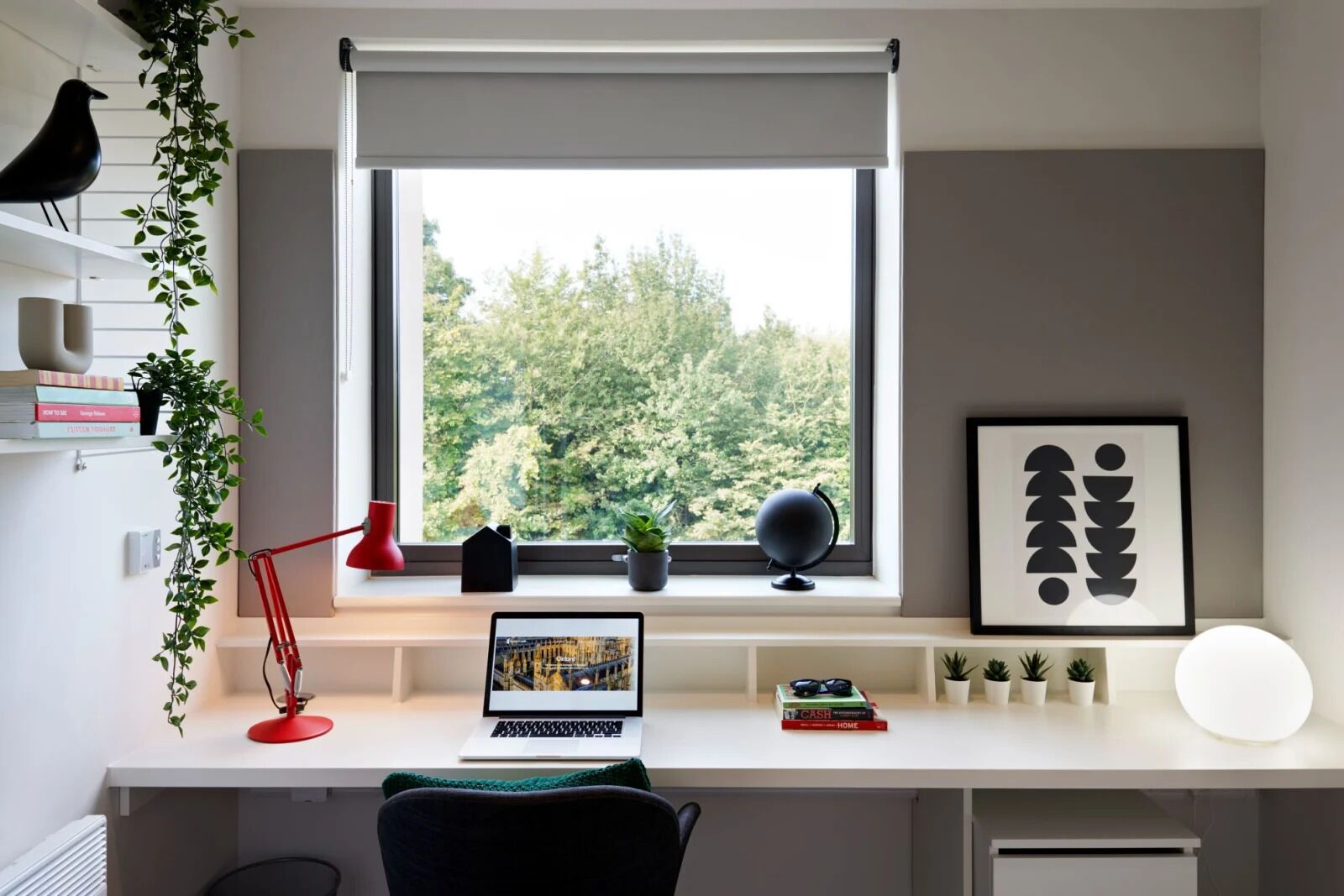 A modern workspace with a laptop, books, a globe, and a framed abstract art piece.