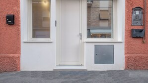 Una puerta blanca con dos ventanas, un buzón y un cuadro eléctrico en una pared rosa con textura.