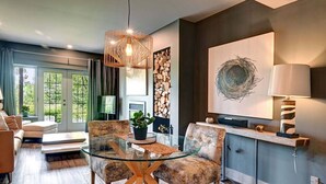 A modern dining area with a glass table, two upholstered chairs, and a hanging light fixture. - The Nest at Algonquin: Retreat for 2 on Mountain (Mont-Tremblant)