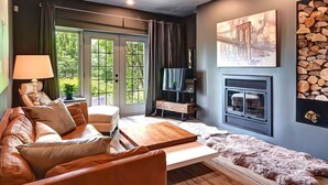 A modern living room with a leather sofa, a wooden coffee table, a fireplace, and a large window with curtains. - The Nest at Algonquin: Retreat for 2 on Mountain (Mont-Tremblant)