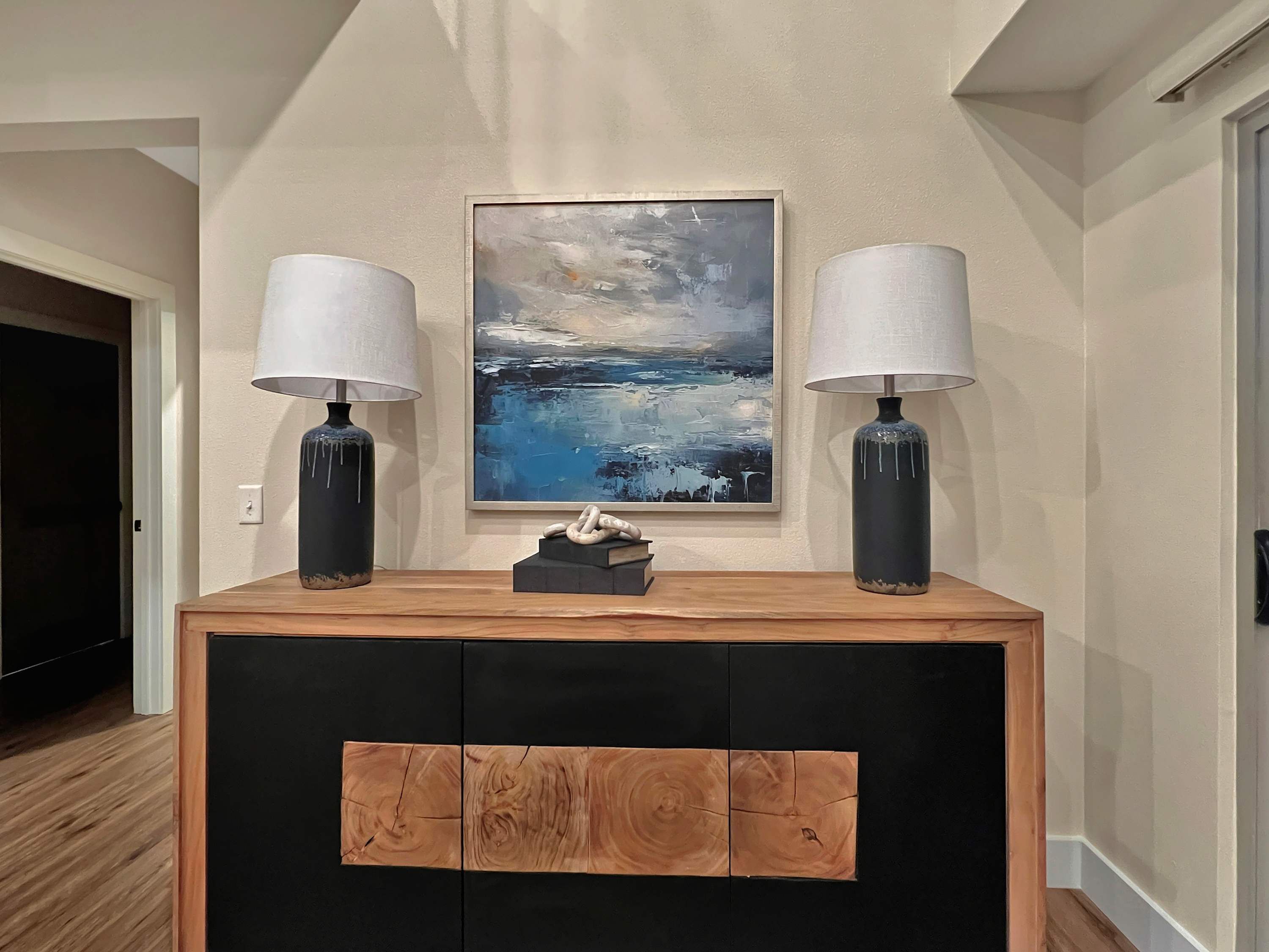 Un salon moderne avec une console en bois, deux lampes et un tableau accroché au mur.
