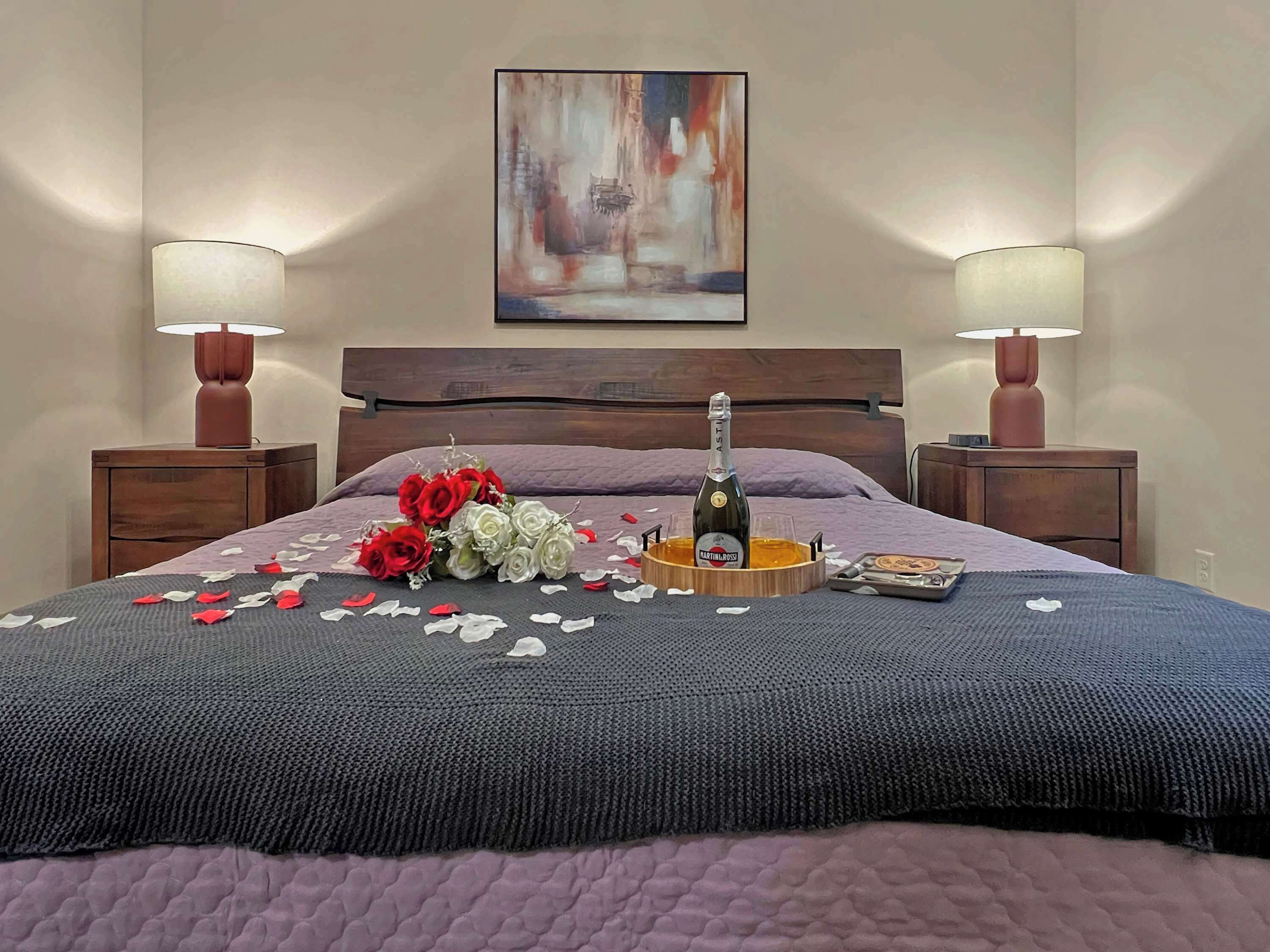 Un lit bien fait, agrémenté d’un bouquet de fleurs, d’une bouteille de champagne et d’un plateau sur lequel repose un livre.