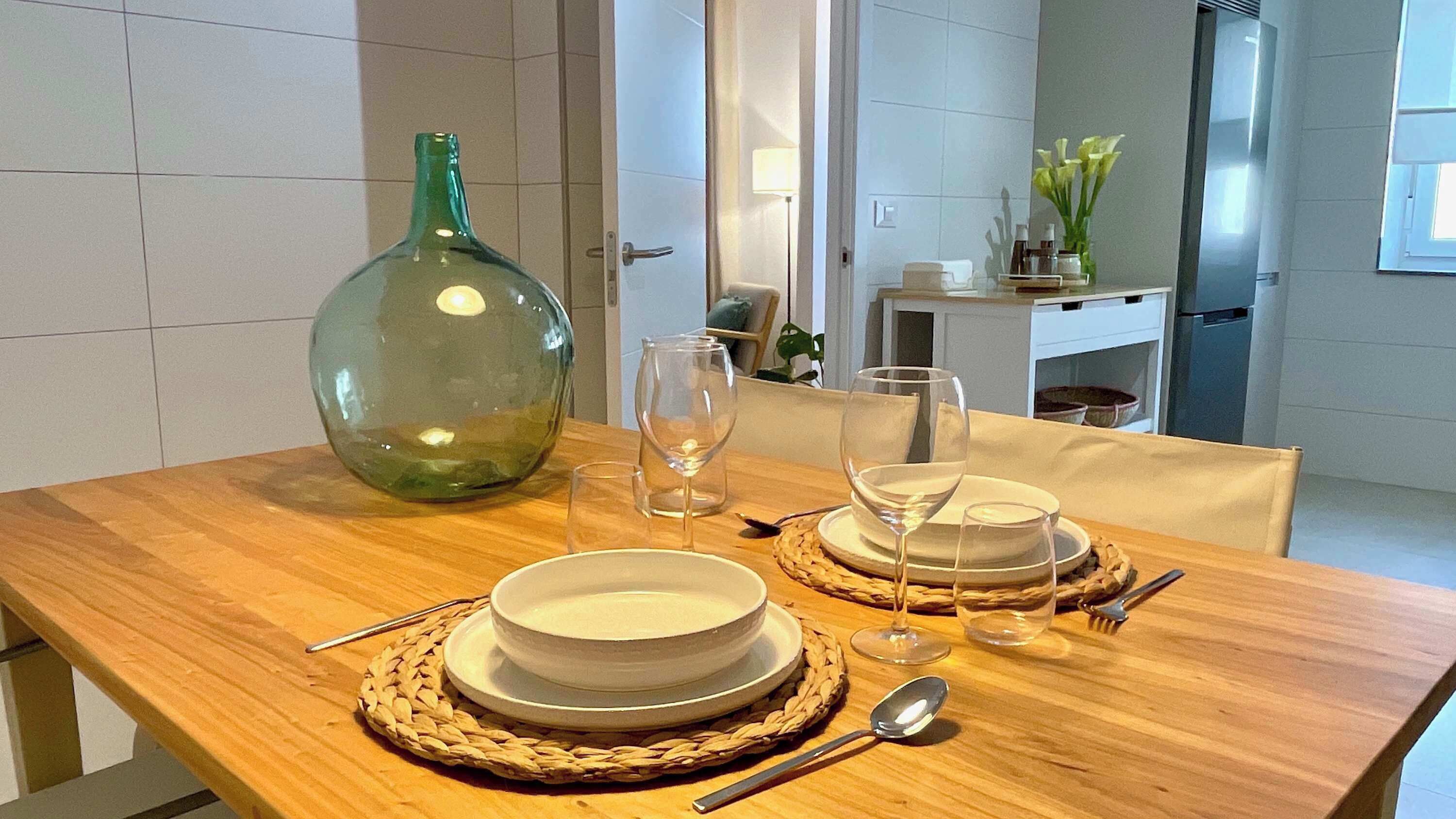 A dining table set with white plates, bowls, and cutlery, a green vase, and two wine glasses.