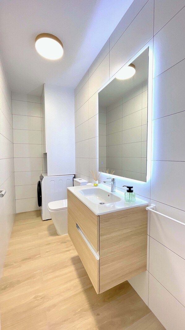 A modern bathroom with a white vanity, a large mirror, and a toilet.