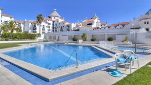 A swimming pool with a diving board, surrounded by white buildings with red-tiled roofs. - Marina Secret in Vilamoura (Loulé)