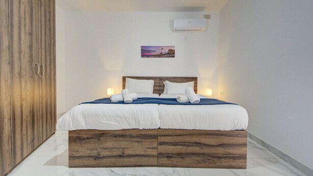 Une chambre à coucher avec un cadre de lit en bois, du linge de lit blanc, une table de chevet, un appareil de climatisation et un tableau accroché au mur.