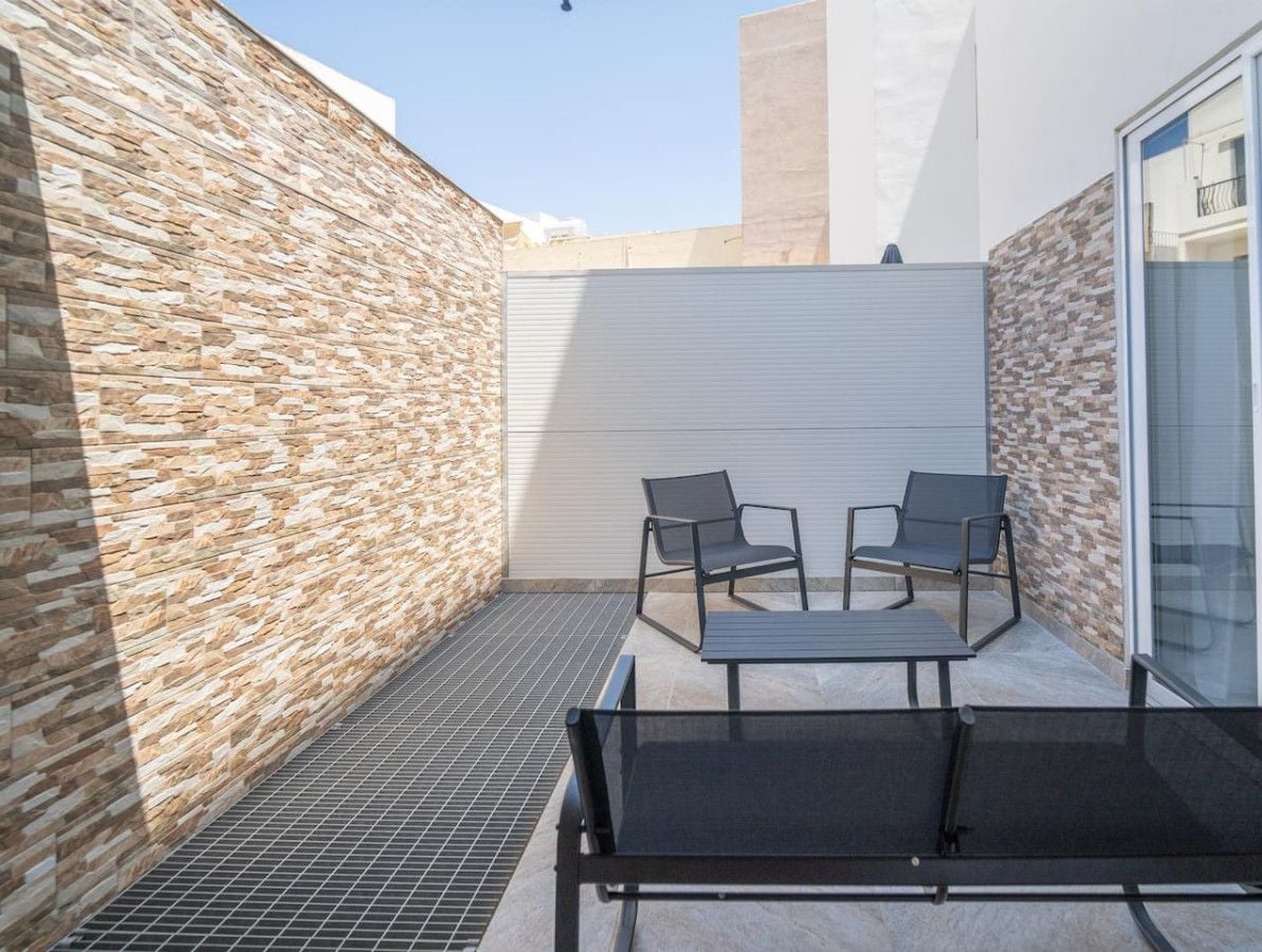 Een modern buitenterras met stenen muren, een uitschuifbaar dak en een zithoek met twee stoelen en een tafel.