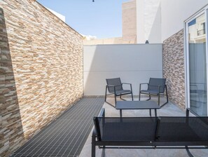 Un patio exterior moderno con paredes de piedra, techo retráctil y un área de estar con dos sillas y una mesa.