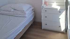 A bedroom with a bed, a dresser, and a hanging light fixture.