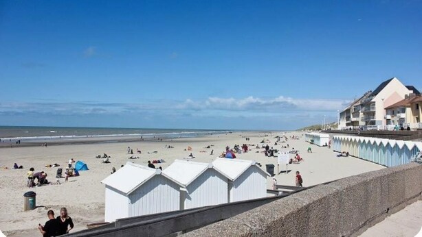 A beach with white beach huts and a building with balconies.