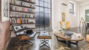 Een ruime kamer met een grote boekenkast, lederen meubels en een uitzicht door een groot raam.