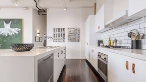 Een moderne keuken met witte kasten, een vaatwasser, oven en kookplaat. Op de muur hangen afbeeldingen in lijsten en op het aanrecht staat een decoratieve schaal.