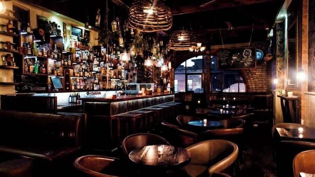 Een bar met houten meubels, hangende lampen en een bakstenen muur.