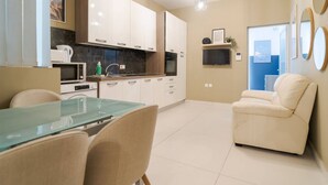 Een moderne keuken met witte kastjes, een glazen eettafel en een beige fauteuil.