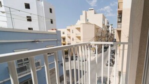 Een balkon met een witte reling, met uitzicht op een straat met geparkeerde auto's en gebouwen.