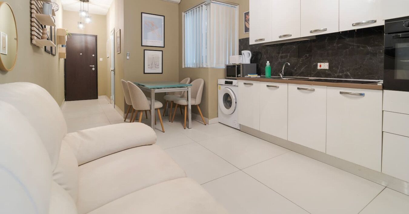 Un espacio habitable compacto con sofá, una mesa de comedor con sillas, lavadora y una zona de cocina con armarios y encimera.