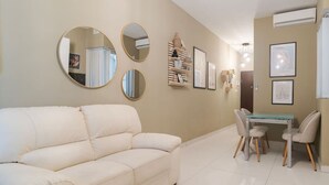 Een woonkamer met een beige bank, een eettafel met stoelen en drie spiegels aan de muur.