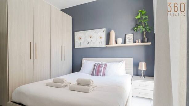 Een moderne slaapkamer met een groot bed, een nachtkastje, een wandplank met decoratieve objecten en een garderobe.