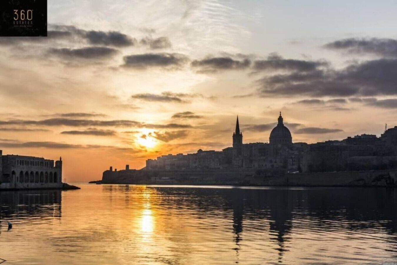 Un coucher de soleil sur une ville, avec un dôme imposant et une promenade au bord de l’eau.