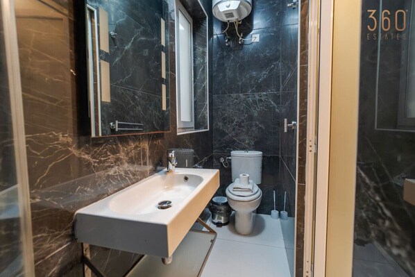 Un baño moderno con lavamanos de mármol, inodoro y ducha.