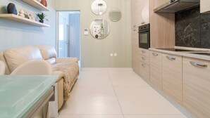 A modern kitchen with light wood cabinets, a black countertop, and a built-in oven. There is a beige sofa with a fur throw and a glass table in the living area. - Lovely fully equipped 1BR APT in Gzira w/WIFI & AC (Gżira)