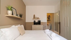 A hotel room with a bed, a TV on a dresser, a closet, and a shelf with plants. - Lovely fully equipped 1BR APT in Gzira w/WIFI & AC (Gżira)