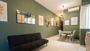 A modern living room with a black sofa, a dining table with chairs, and a kitchen area with a white refrigerator. - Cosy 1BR fully equipped Apt with balcony w/WIFI ! (Gżira)